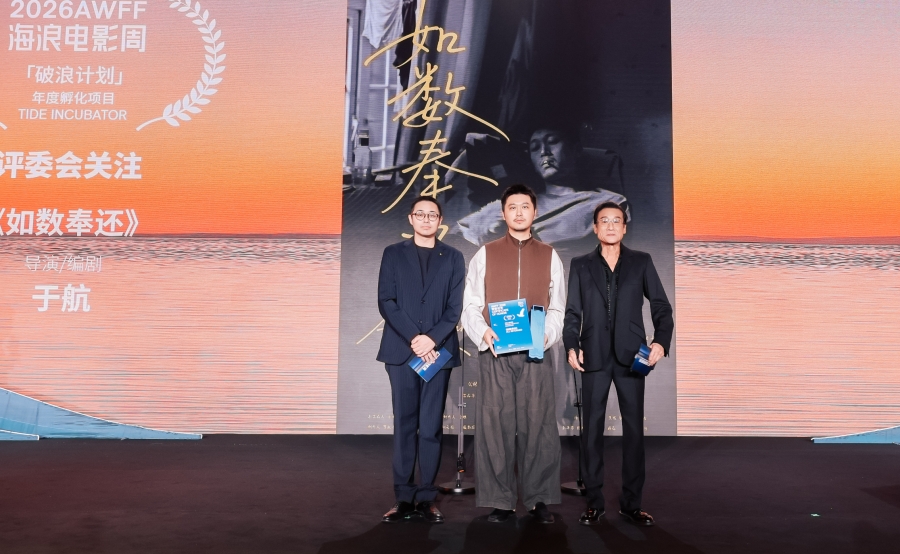 Aranya Waves Film Festivali sahnesinde ödül alan üç kişi poster önünde poz veriyor
