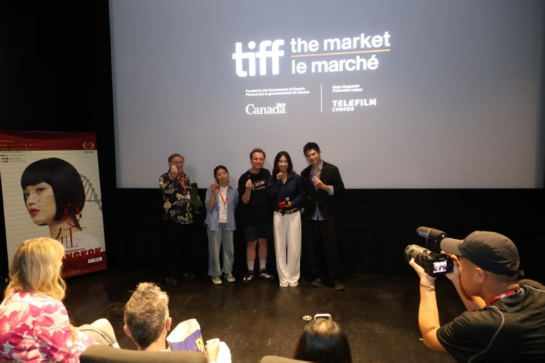 TIFF logosu önünde ayakta duran ekip, salondaki fotoğrafçı ve film afişi görünür