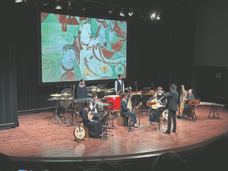 Dunhuang görselleri önünde geleneksel çalgılar çalan müzisyenler sahnede performans sergiliyor