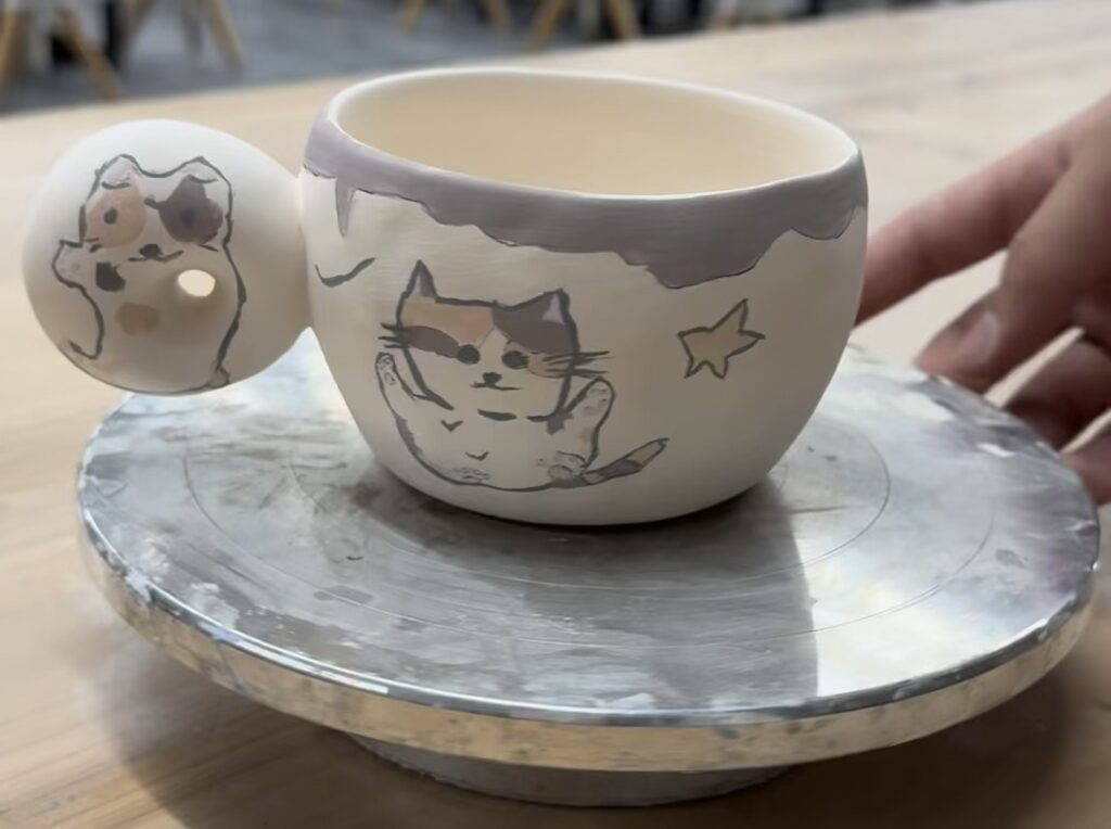 Kedi çizimleriyle süslenmiş el yapımı seramik fincan döner tabla üzerinde duruyor