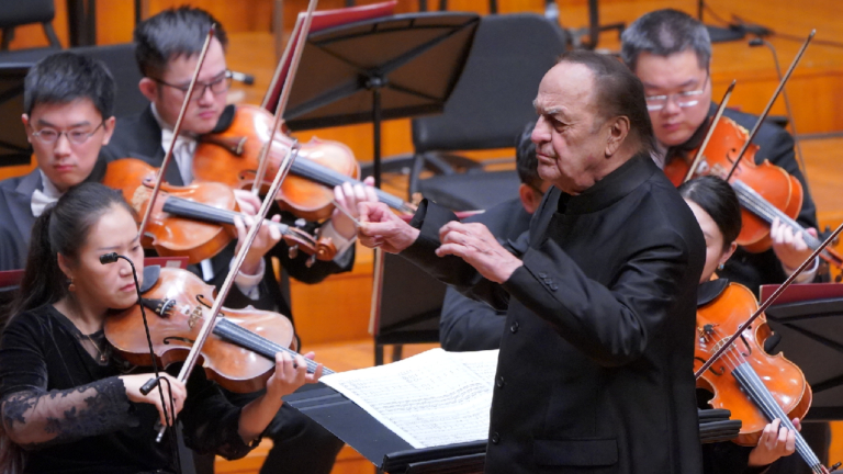 Orkestra şefi, yaylı çalgılar topluluğunu yönetirken müzisyenler enstrümanlarıyla performans sergiliyor