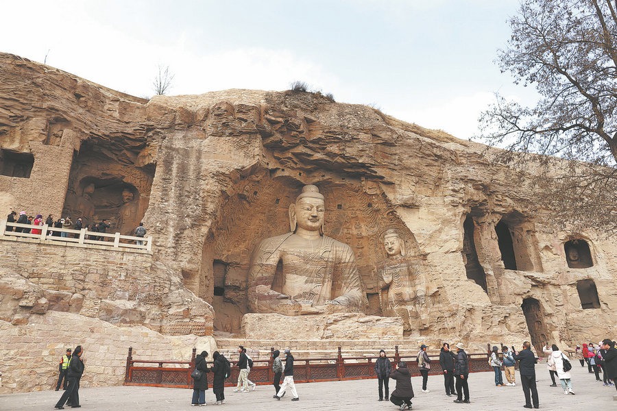 Yungang Mağaraları’nda kayaya oyulmuş büyük Buda heykelleri ve ziyaretçiler görülüyor