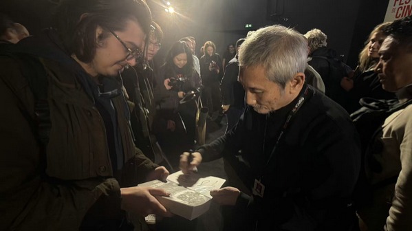 Tsui Hark kalabalık bir etkinlikte hayranının getirdiği nesneyi imzalıyor