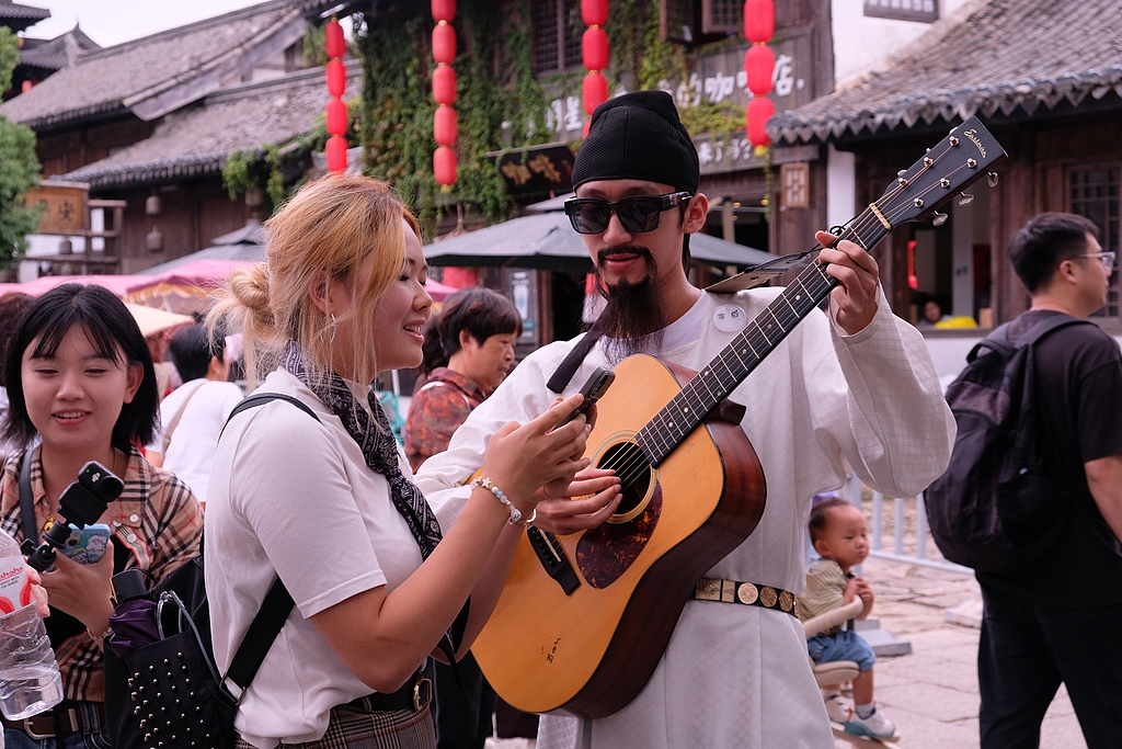 Tarihi bir sokakta turist, geleneksel kıyafetli müzisyenle gitar performansına eşlik ediyor