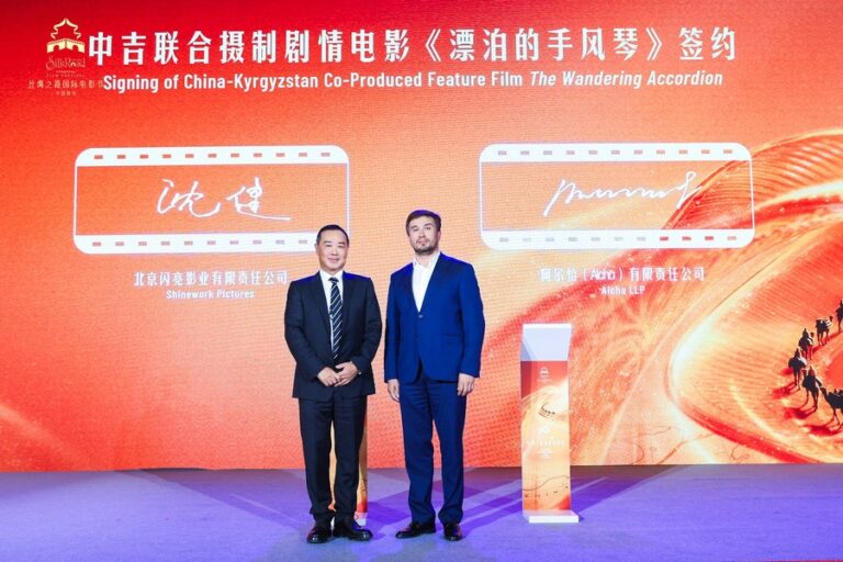 Xi’an’daki imza töreninde iki erkek, Gezgin Akordeonlar filminin Çin-Kırgızistan ortak yapım afişi önünde duruyor.