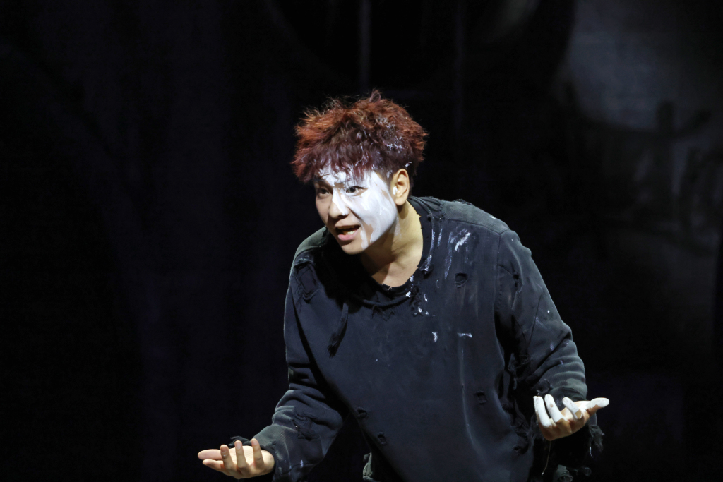 Sahne ışıkları altında Hamlet rolündeki oyuncu, yoğun ve dramatik bir performans sergiliyor.