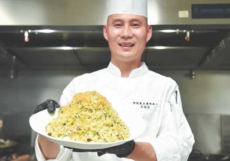 Beyaz üniformalı bir şef, büyük tabakta Yangzhou kızarmış pilavı sunuyor.