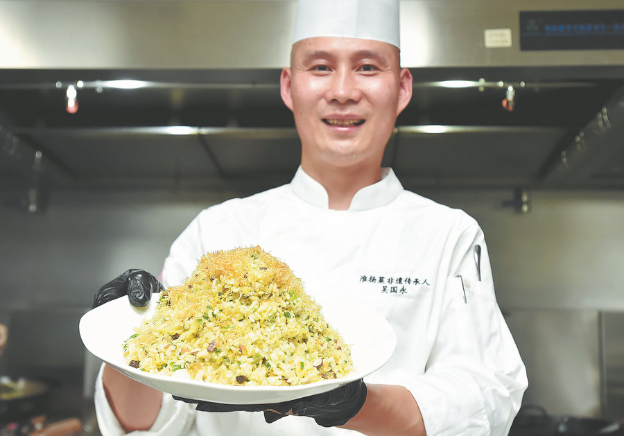 Beyaz üniformalı bir şef, büyük tabakta Yangzhou kızarmış pilavı sunuyor.